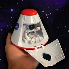 a hand holding a toy space shuttle in it's left side, with the astronaut inside