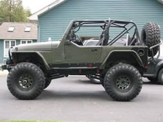 a green jeep parked in front of a blue building with two large tires on it