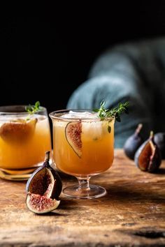 two glasses filled with drinks sitting on top of a wooden table next to figs