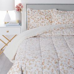 a bed with a white and gold comforter next to a night stand