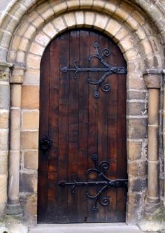 an arched wooden door with iron work on the front and side panels, in a stone building