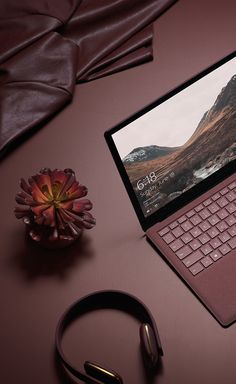 an open laptop computer sitting on top of a desk next to headphones and a flower