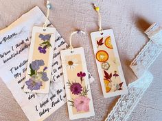 three tags with flowers on them are hanging from a lace doily next to an envelope