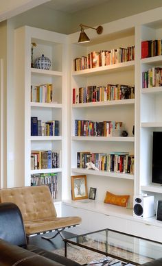 a living room filled with lots of white bookshelves next to a glass coffee table