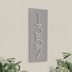 a house number sign mounted to the side of a wall next to potted plants