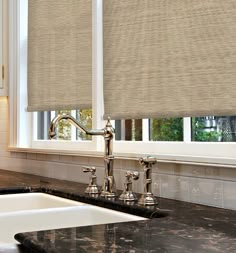 a kitchen sink under a window with roman shades