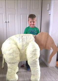 a young boy standing next to an elephant made out of paper mache and cardboard