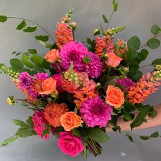 a woman holding a bouquet of flowers in her hand with orange and pink blooms on it