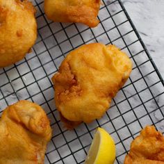 four fried fish on a wire rack with lemon wedges and sauce in the background