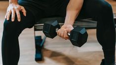 a man sitting on a bench holding two black dumbbells