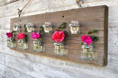 mason jars filled with pink and red flowers hang on a wall