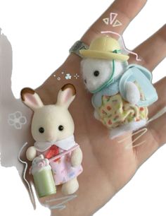 two small stuffed animals sitting on top of a person's hand next to each other