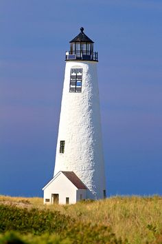 a white lighthouse on top of a hill with blue sky in the backgroud