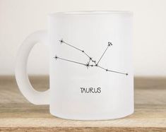 a white coffee mug with the zodiac sign taurus on it sitting on a wooden table