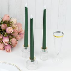 three candles are sitting next to each other on a table with pink flowers and glass vases