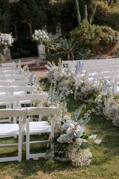 an outdoor ceremony setup with white chairs and blue flowers on the grass in front of it