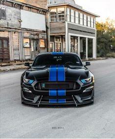 a black mustang with blue stripes parked in front of an old building on the street