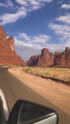 a car driving down a desert road with mountains in the background and clouds in the sky