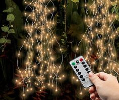 a hand holding a remote control in front of a string of lights that are hanging from the ceiling