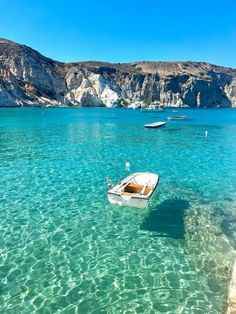 a small boat floating on top of a blue ocean next to a rocky cliff face