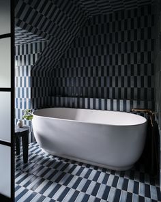 a white bath tub sitting inside of a bathroom next to a black tiled wall and floor