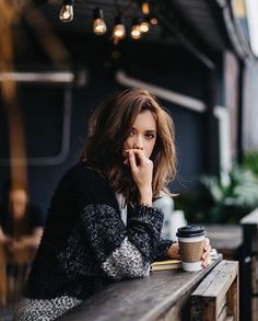 a woman sitting at a table with a cup of coffee in her hand and looking off into the distance