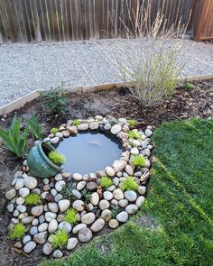 a small pond in the middle of a garden with rocks and gravel around it, surrounded by grass