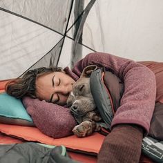 a woman laying on top of a sleeping bag next to a dog