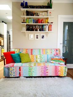 a living room with a colorful couch and bookshelves on the wall above it