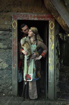 a man and woman standing in an outhouse holding a teddy bear while wearing medieval clothing