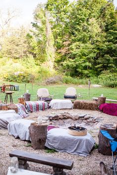 there is a fire pit in the middle of a field with chairs and blankets around it