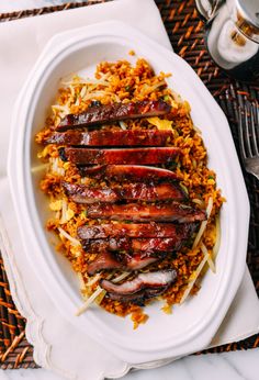 a white plate topped with meat and rice on top of a woven place mat next to a fork