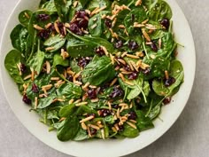 spinach salad with cranberries and almonds in a white bowl on a table