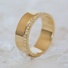 a gold wedding ring with small diamonds on it's side, sitting on a white surface