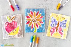 three square drawings with colored crayons and markers on the ground next to them