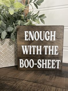 a wooden sign that says enough with the boo - sheet on it next to a potted plant