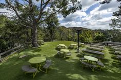 an outdoor picnic area with tables and benches on the grass, surrounded by trees in the background