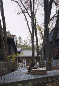 four people sitting on a bench in front of some trees and house with one person standing