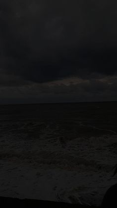 a person standing in front of the ocean under a dark sky with storm clouds above them