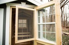 an open window on the side of a house with wood siding and mesh coverings