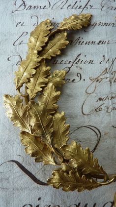 a gold leaf brooch sitting on top of a piece of paper with writing in the background