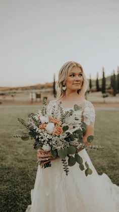 a woman in a white dress holding a bouquet of flowers and greenery on her wedding day