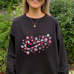 a woman wearing a black nike sweatshirt with pink and blue flowers on the front, smiling at the camera