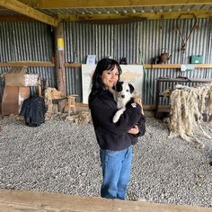 a woman holding a cat in her arms while standing next to a pile of wood