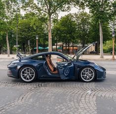 a blue sports car is parked on the side of the road with its door open