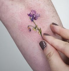 a close up of a person's hand holding a flower tattoo on her arm