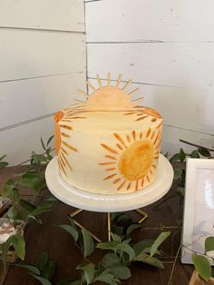 a white cake sitting on top of a wooden table next to a framed photo and greenery