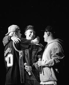 three men standing next to each other in front of a black and white photo with one holding a microphone