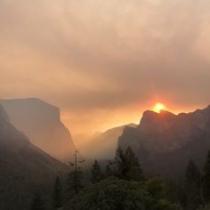 the sun is setting over some mountains and trees