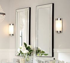 a bathroom vanity with two mirrors above it and flowers in vases on the counter